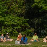 woman seated on the ground in the grass on blanket talking to adults, also seated